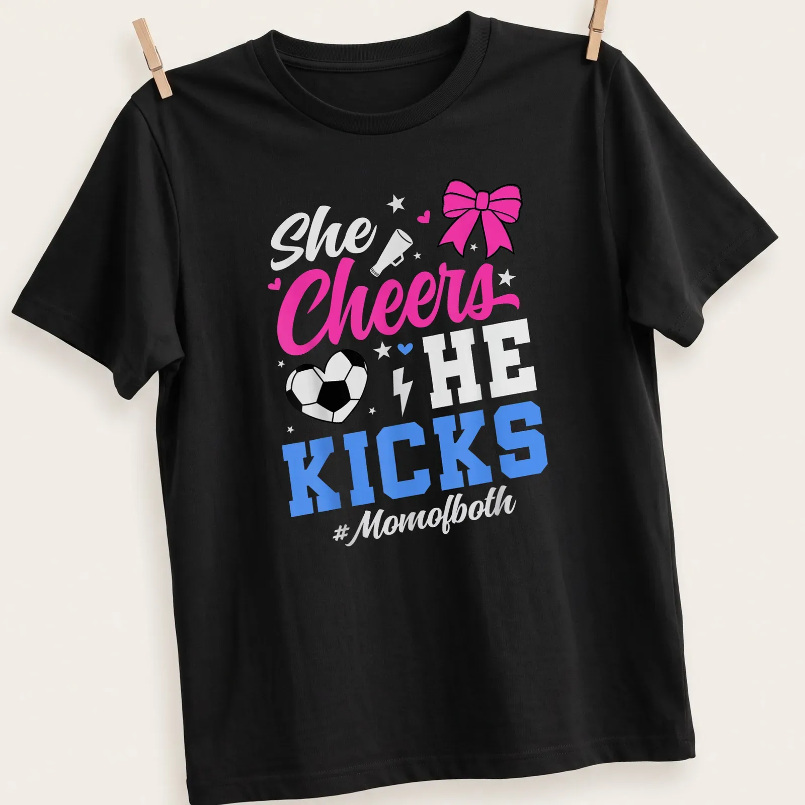 Colorful shirt with text 'She Cheers He Kicks #Momofboth' and graphics of pom-poms and a soccer ball — printed on a unisex t-shirt