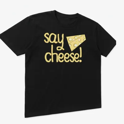 Playful cartoon cheese with text 'say cheese!' in yellow tones — printed on a unisex t-shirt (angled view)
