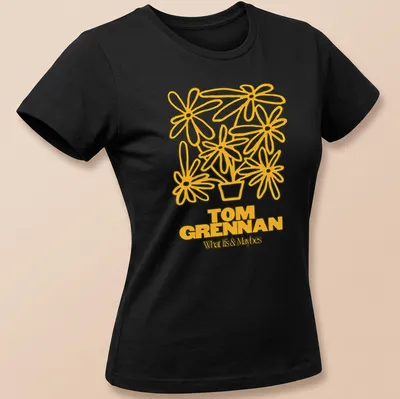Line art illustration of a flower pot with flowers and text 'TOM GRENNAN What Is & Maybes' — printed on a women's shirt