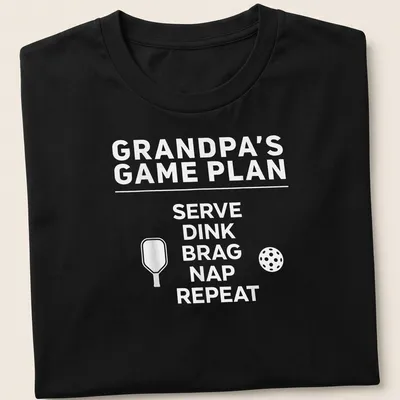 Bold typography design with the phrase Grandpa's Game Plan Serve Dink Brag Nap Repeat — printed on a unisex t-shirt