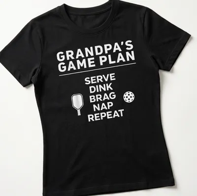 Bold typography design with the phrase Grandpa's Game Plan Serve Dink Brag Nap Repeat — printed on a women's shirt