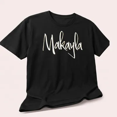 Elegant script t-shirt featuring the name Makayla in gold on white — printed on a unisex t-shirt (angled view)