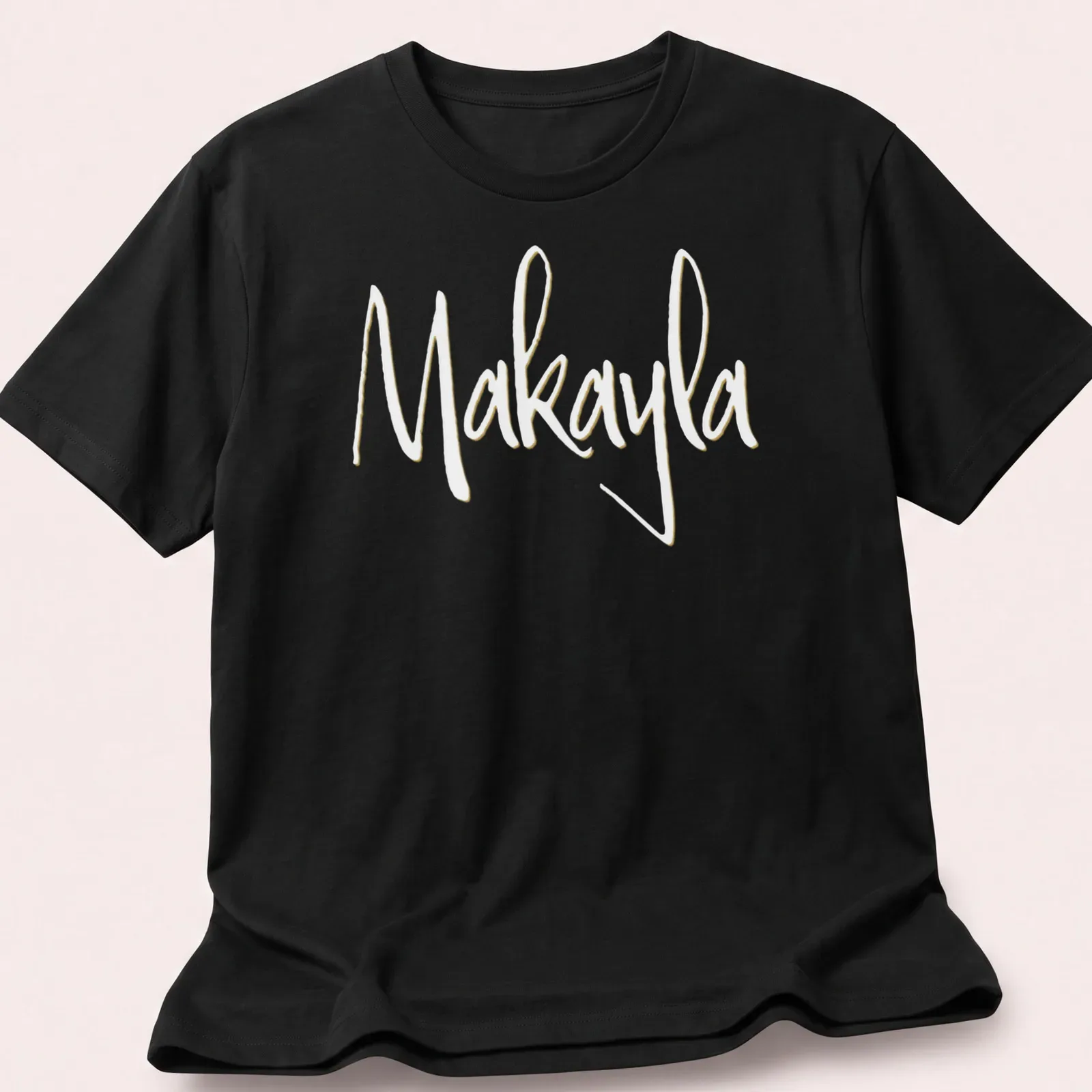 Elegant script t-shirt featuring the name Makayla in gold on white — printed on a unisex t-shirt