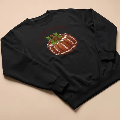 Cartoon pumpkin with footballs and the text 'TIS THE SEASON' in festive colors — printed on a unisex sweatshirt